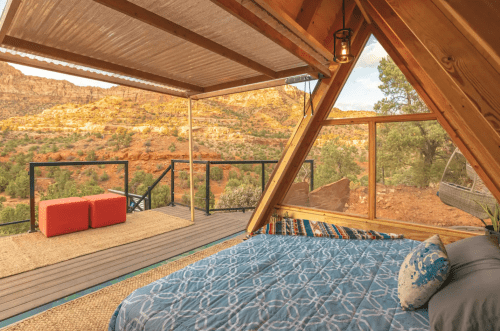 Cozy A-frame cabin interior with a bed, overlooking a scenic desert landscape through large windows.